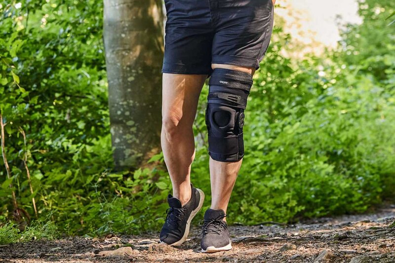 Beskåret bilde av en person i et skogsmiljø med en CROSS semi-rigid kneortose for hyperekstensjon av kneleddet.