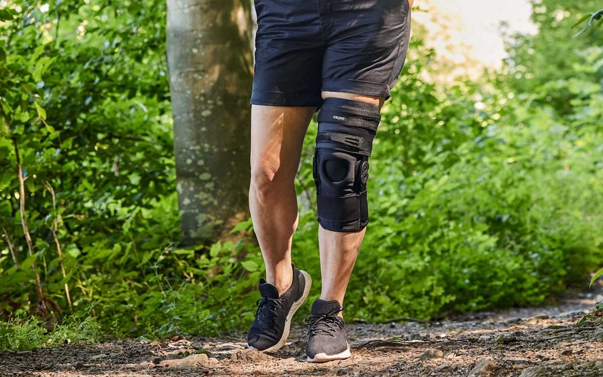 Beskåret bilde av en person i et skogsmiljø med en CROSS semi-rigid kneortose for hyperekstensjon av kneleddet.